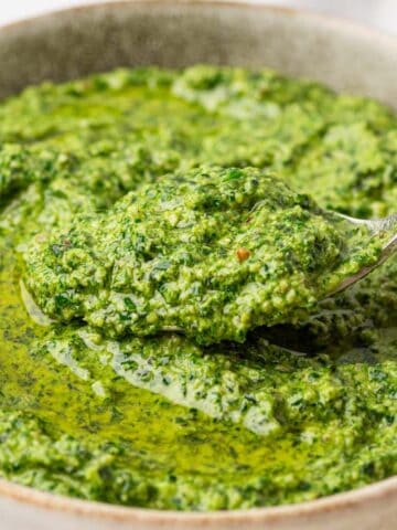 a spoon taking the creamy pesto sauce without pine nuts from a bowl.