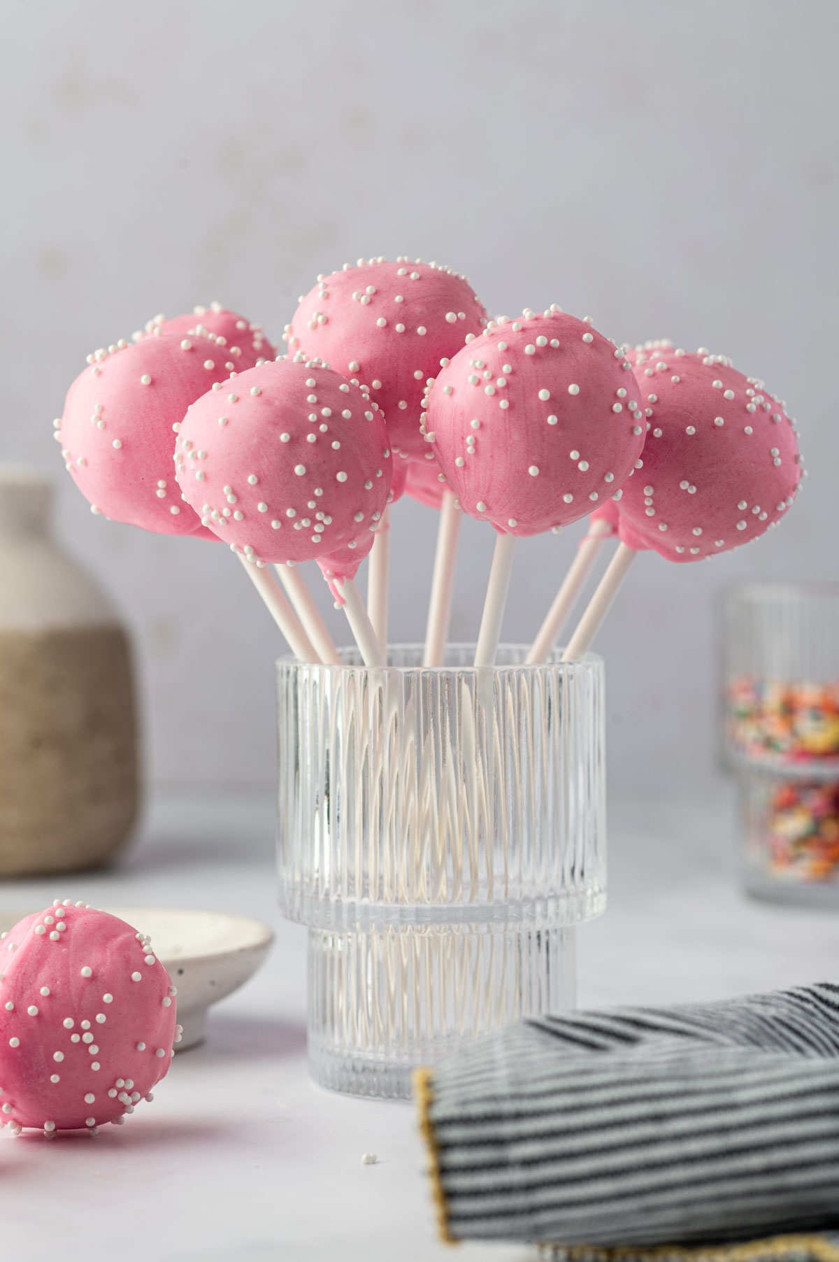 Birthday cake pops cooling on a tall glass after decorating