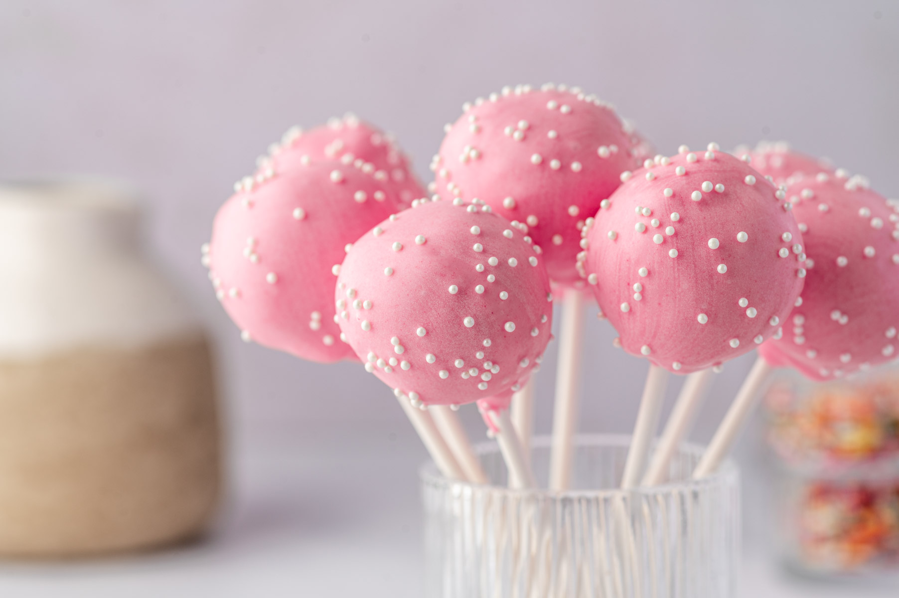 Birthday cake pops with pink candy coating and colorful sprinkles on a glass jar.