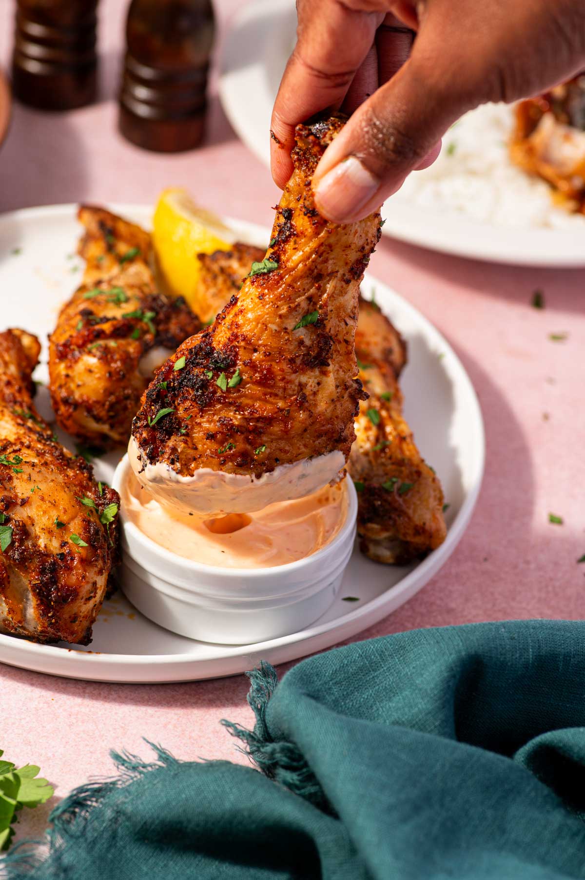Air fried chicken drumsticks being dipped in a sauce.