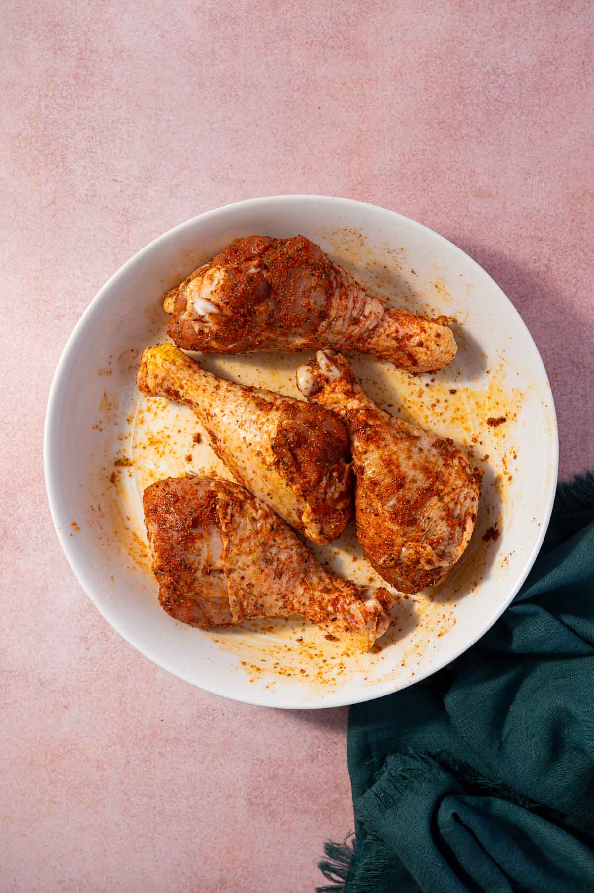 Seasonings are coated well on the chicken drumsticks and placed in a white bowl.