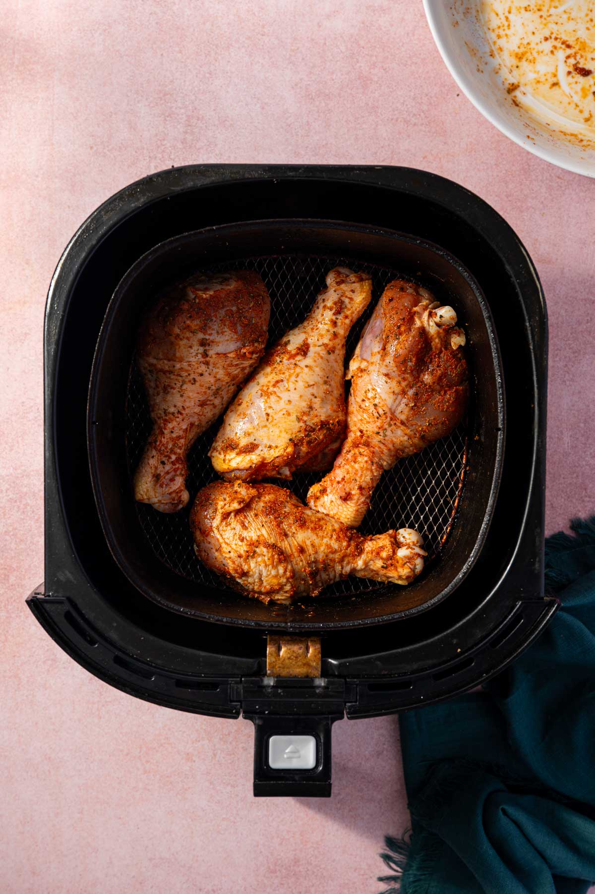 Seasoned chicken drumsticks are placed in an air fryer basket ready to air fry.