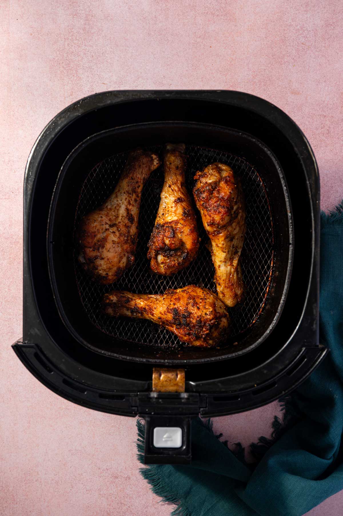 Perfected cooked crispy chicken drumsticks in an air fryer basket.