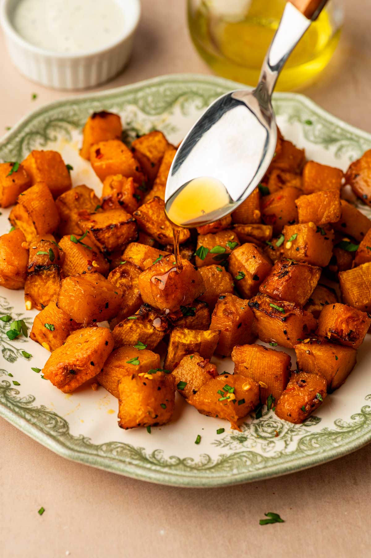 Air Fryer Butternut Squash served in a platel with caramelized edges and fresh parsley. A spoon is drizzling maple syrup on top.