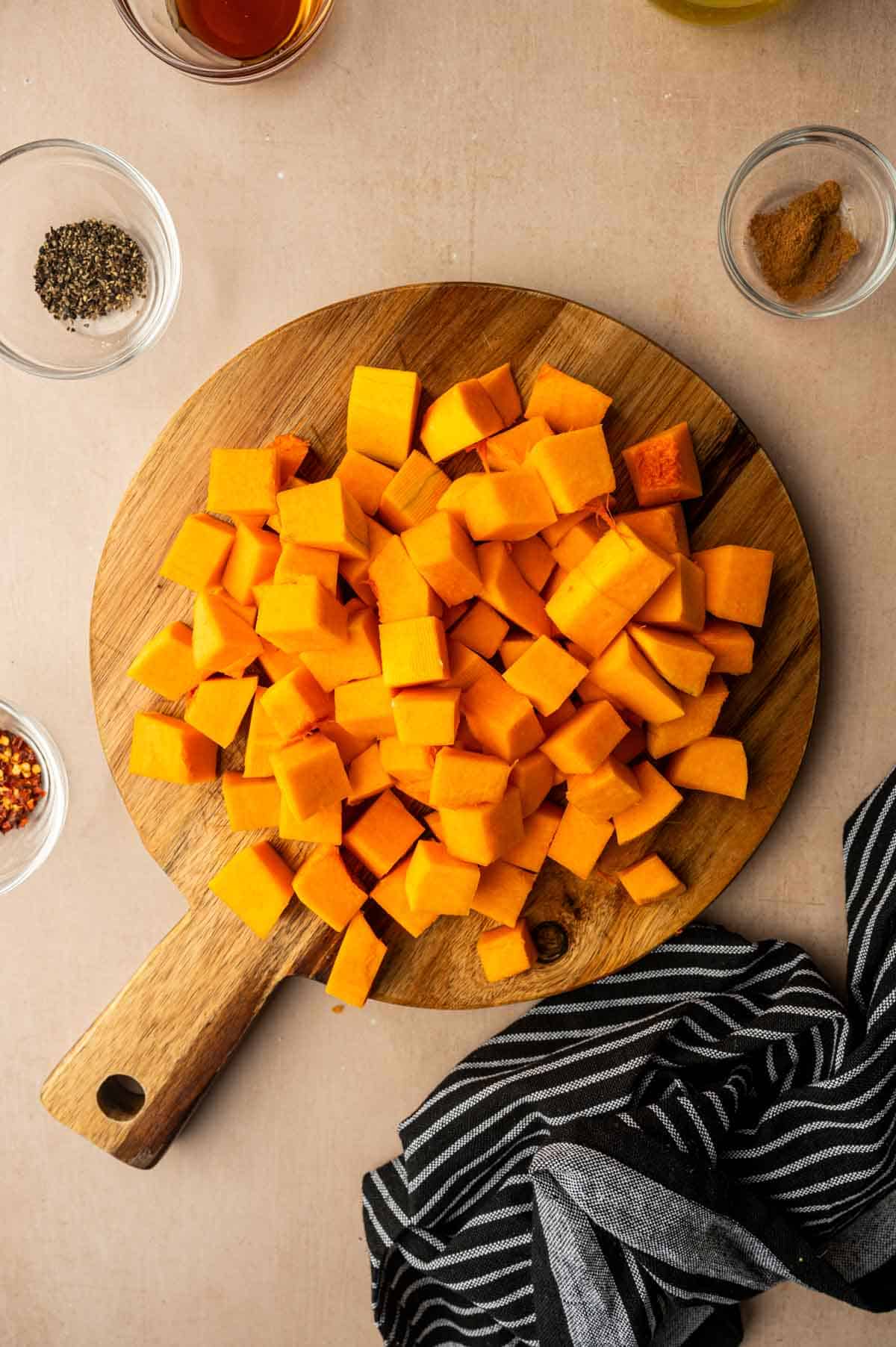 Butternut squash cubes are placed in to a wooden cutting board.