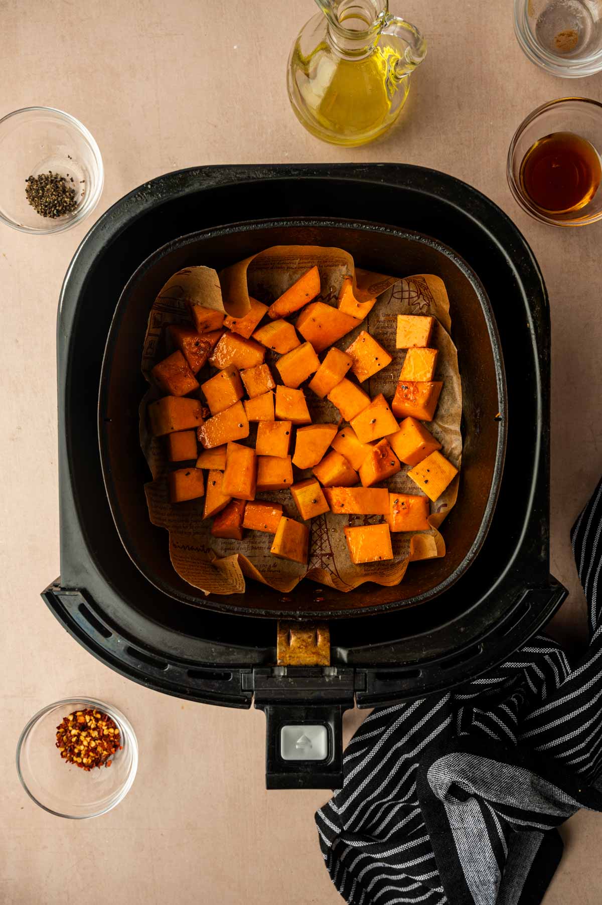 Seasoned butternut squash cubes arranged in an air fryer basket before cooking.
