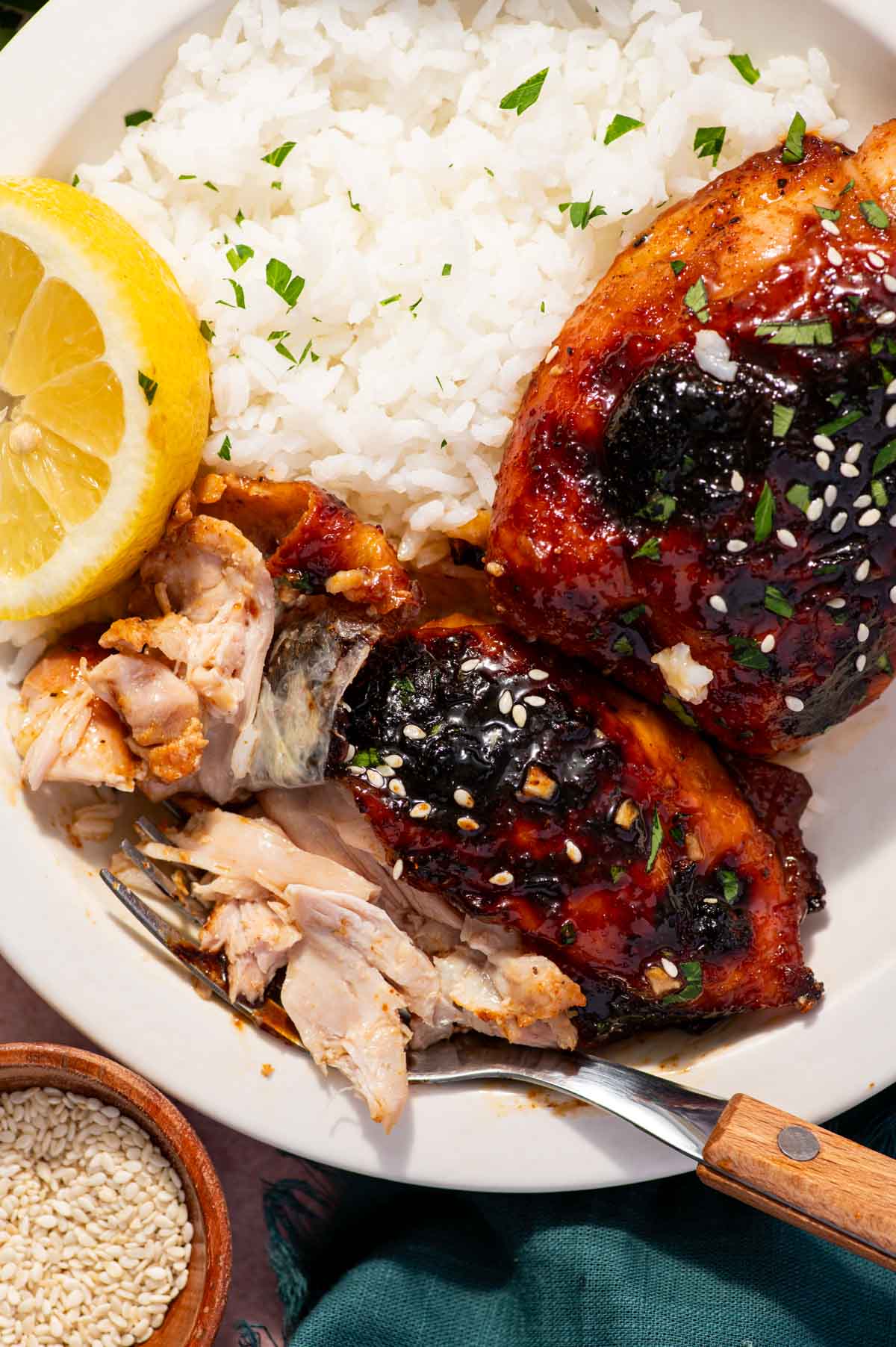 Sticky honey garlic glaze on baked chicken thighs showing the inner flesh of cooked chicken with fork in the side.