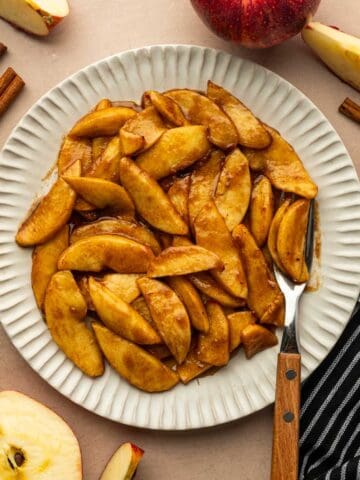 Beautifully caramelized air fryer apple slices placed in a plate with a fork.
