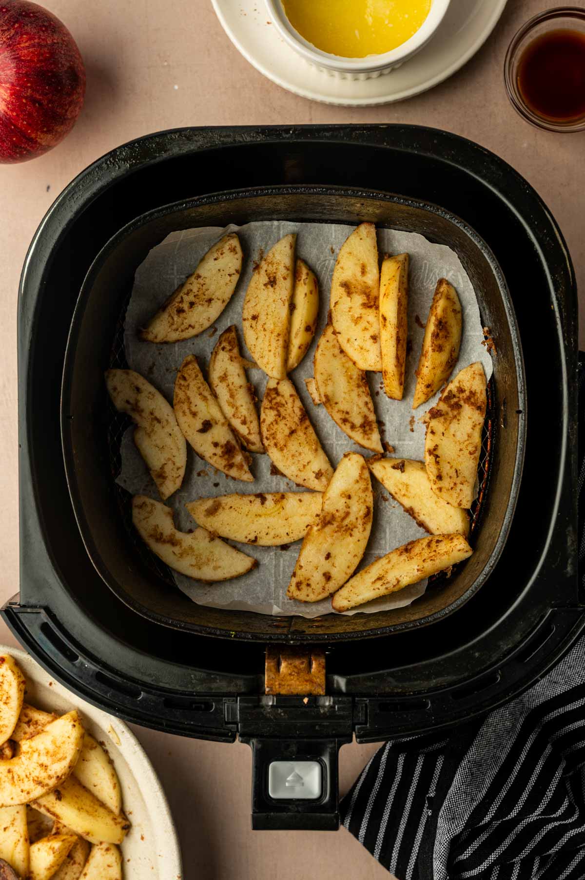 Seasoned apple slices being added to the air fryer basket.