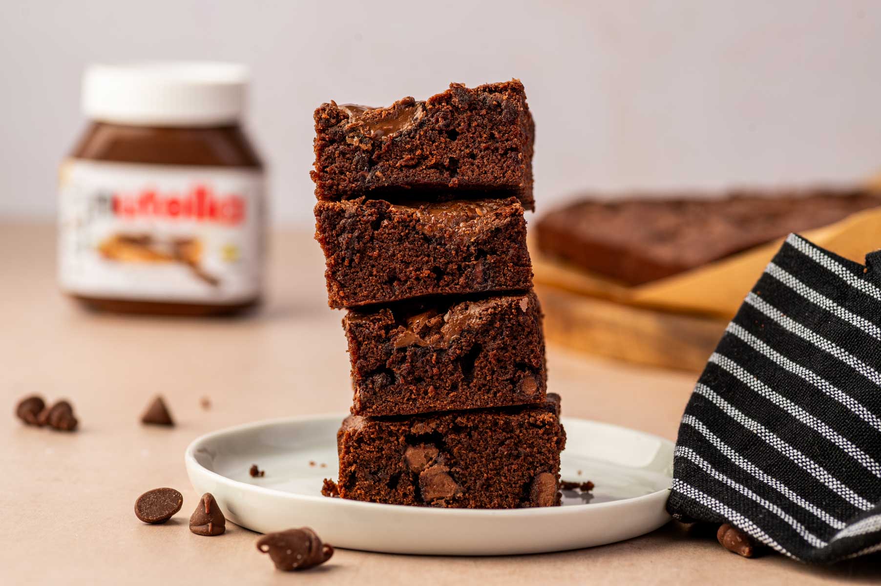 Nutella brownie squares with soft fudgy centers stacked one above the other and nutella bottle in the background.