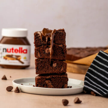 Homemade Nutella brownies cut into squares stacked one above the other and the nutella is drizzling downwards.