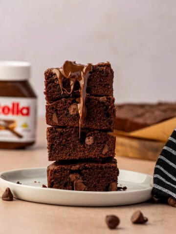 Homemade Nutella brownies cut into squares stacked one above the other and the nutella is drizzling downwards.