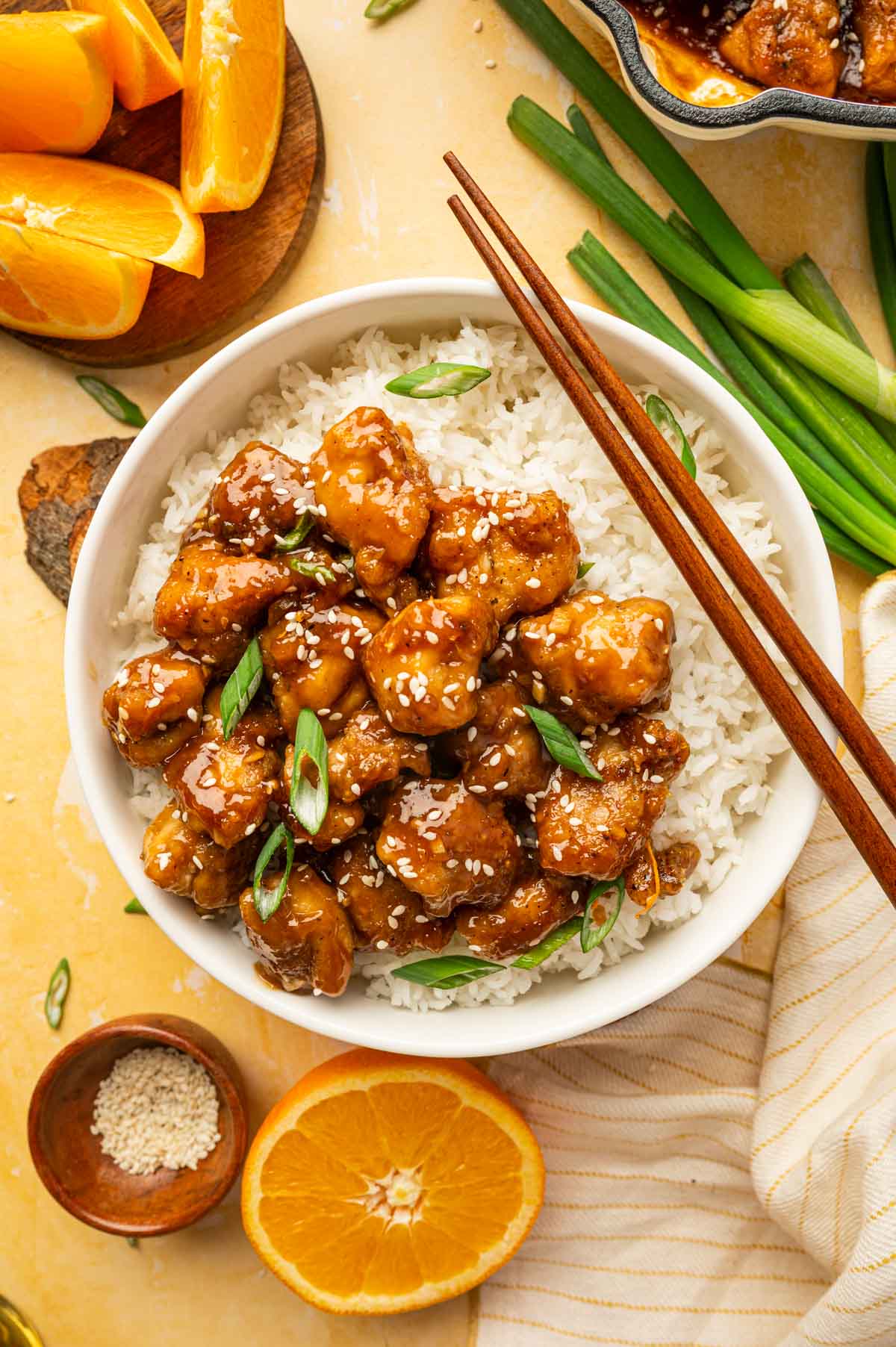 Orange chicken is served alongside with rice. Garnished with green onions and sesame seeds.