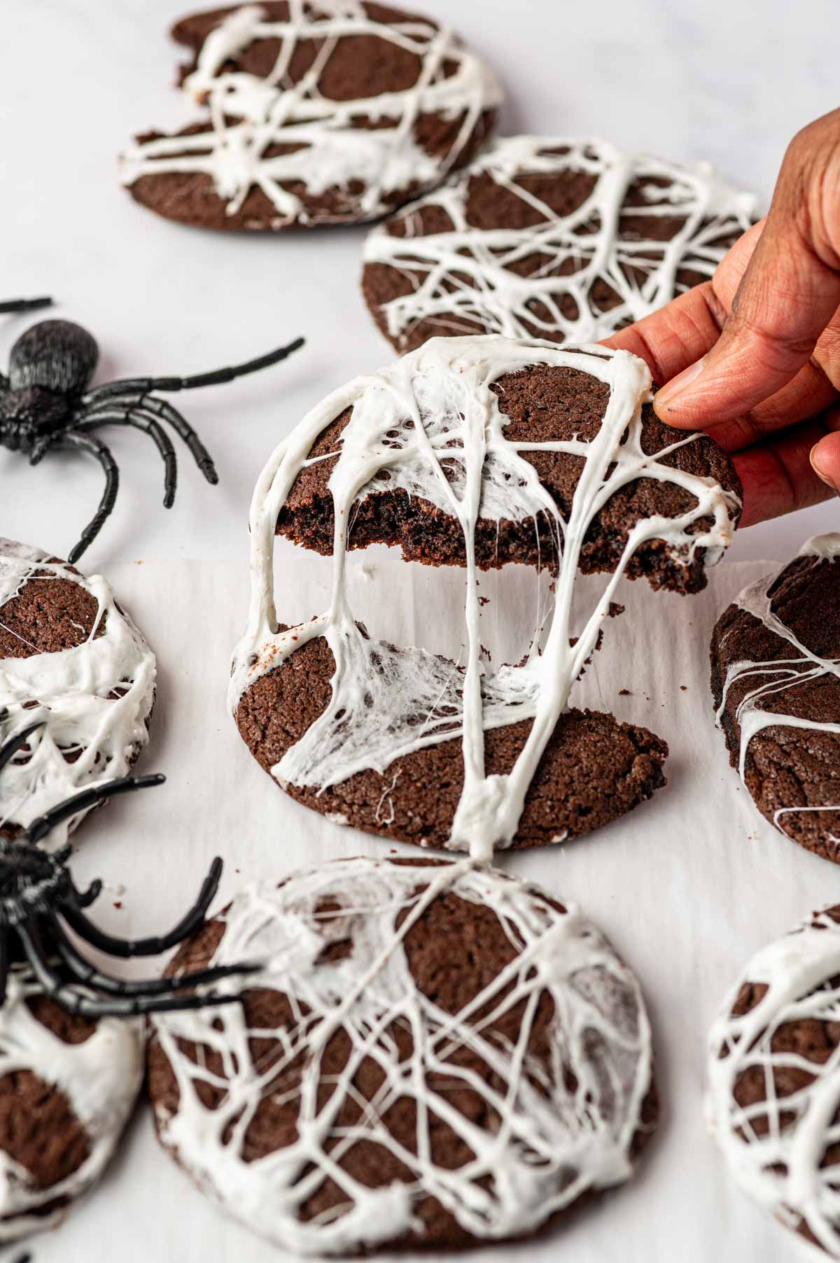 A hand is holding the half of the spider web cookies and marshmallow is melty and gooey.