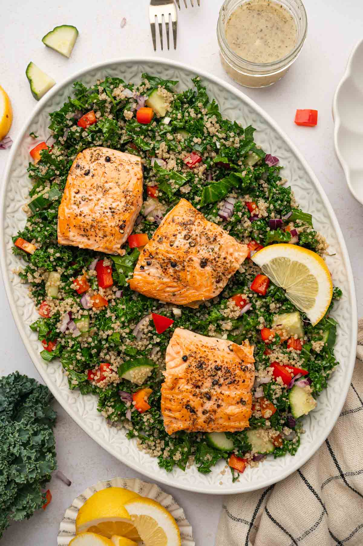 Salmon kale quinoa salad beautifully platted in a oval platter with the dressing in the side.